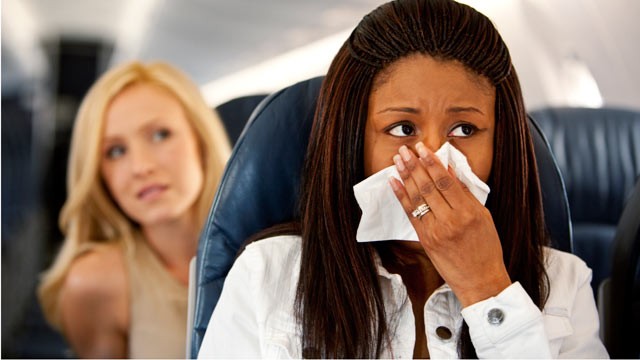A passenger holds a cloth over her nose and mouth as the airplane cabin spraying commences.