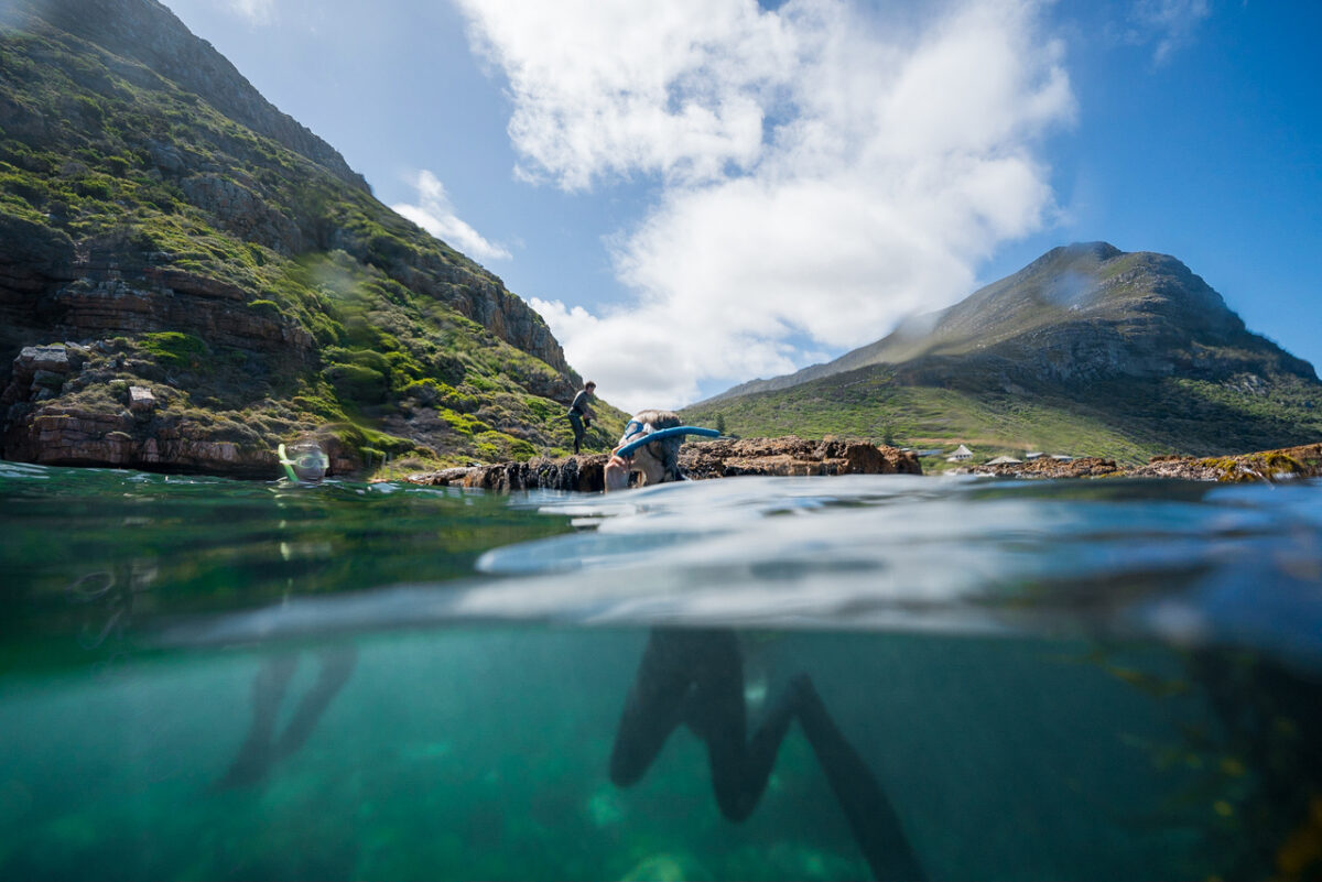 People snorkelling in. Cape Town's blue ocean with a background of the green mountains and blue sky with white cloud. These are the top 5 snorkelling spots in Cape Town