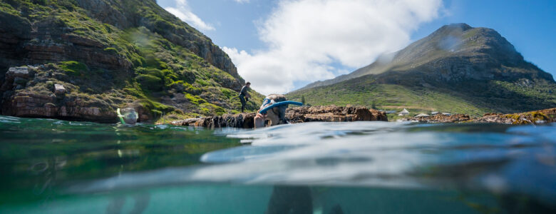 People snorkelling in. Cape Town's blue ocean with a background of the green mountains and blue sky with white cloud. These are the top 5 snorkelling spots in Cape Town