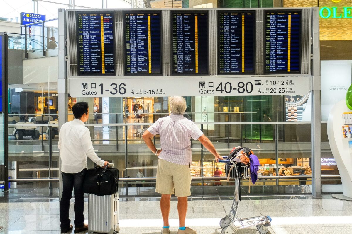 two men in an airport looking at the airline board to see which flights are about to take off