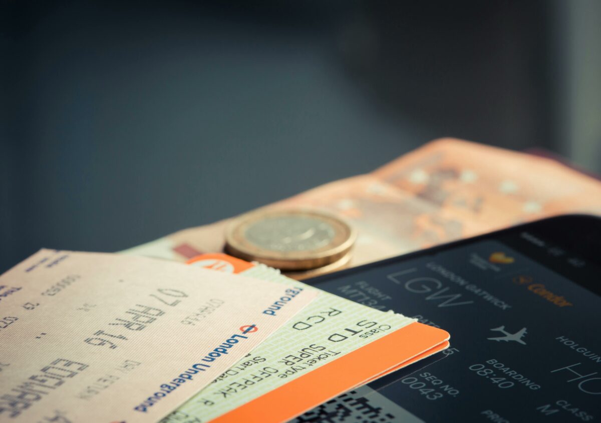 Close-up of travel essentials: flight boarding pass, train tickets, euros, and a phone screen, capturing the cost layers behind why flights are expensive.