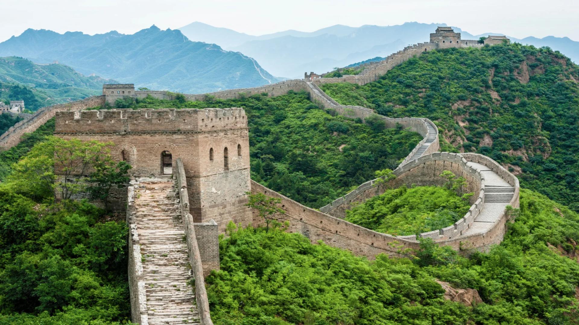 A view of the Great Wall of China, there is a close up of one of the watchtowers. The wall is long and winding into a background of hills and mountains with lush green vegetation around. Top 5 cheap Rand-frienldy travel deals for Black Friday 2025