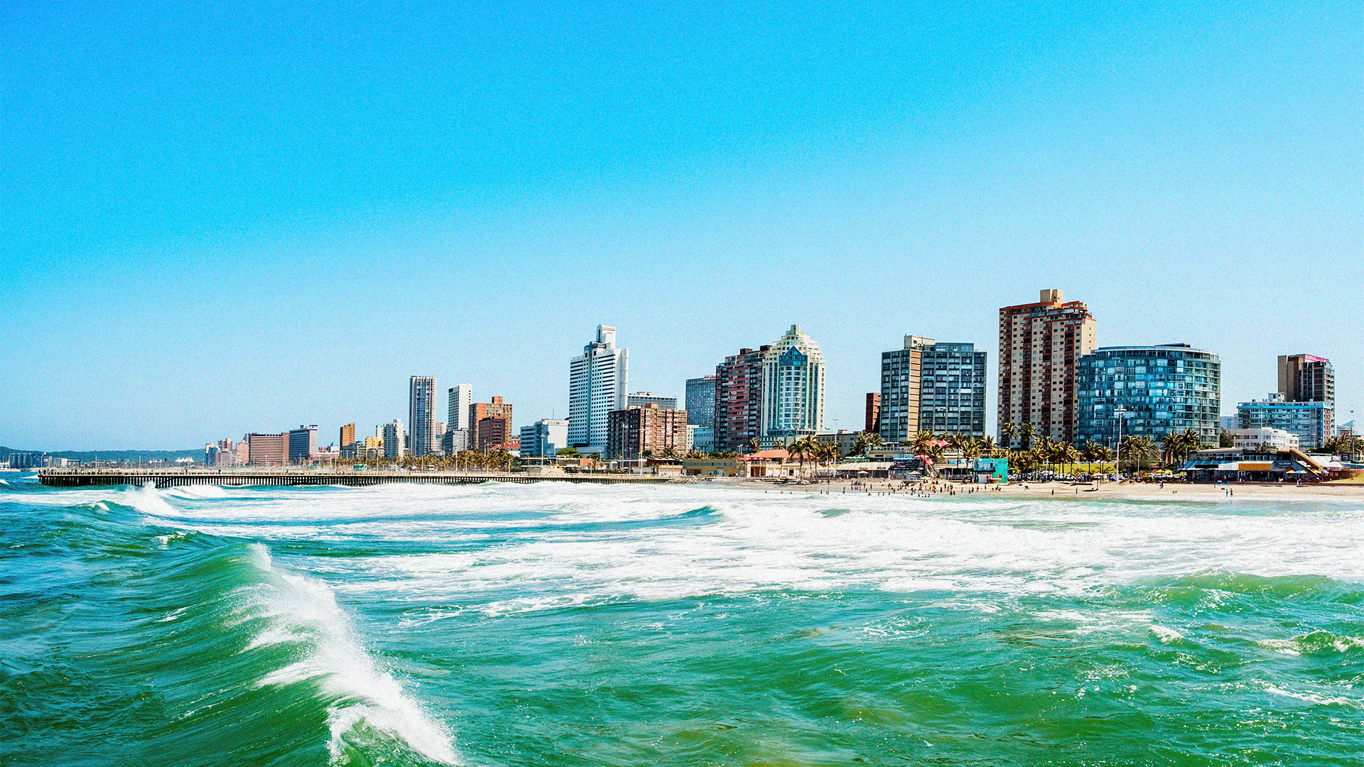 View of the beach waves crashing onto the shore with a foreground of Durban's skyline. Durban is one of the warmest places in South Africa during winter.