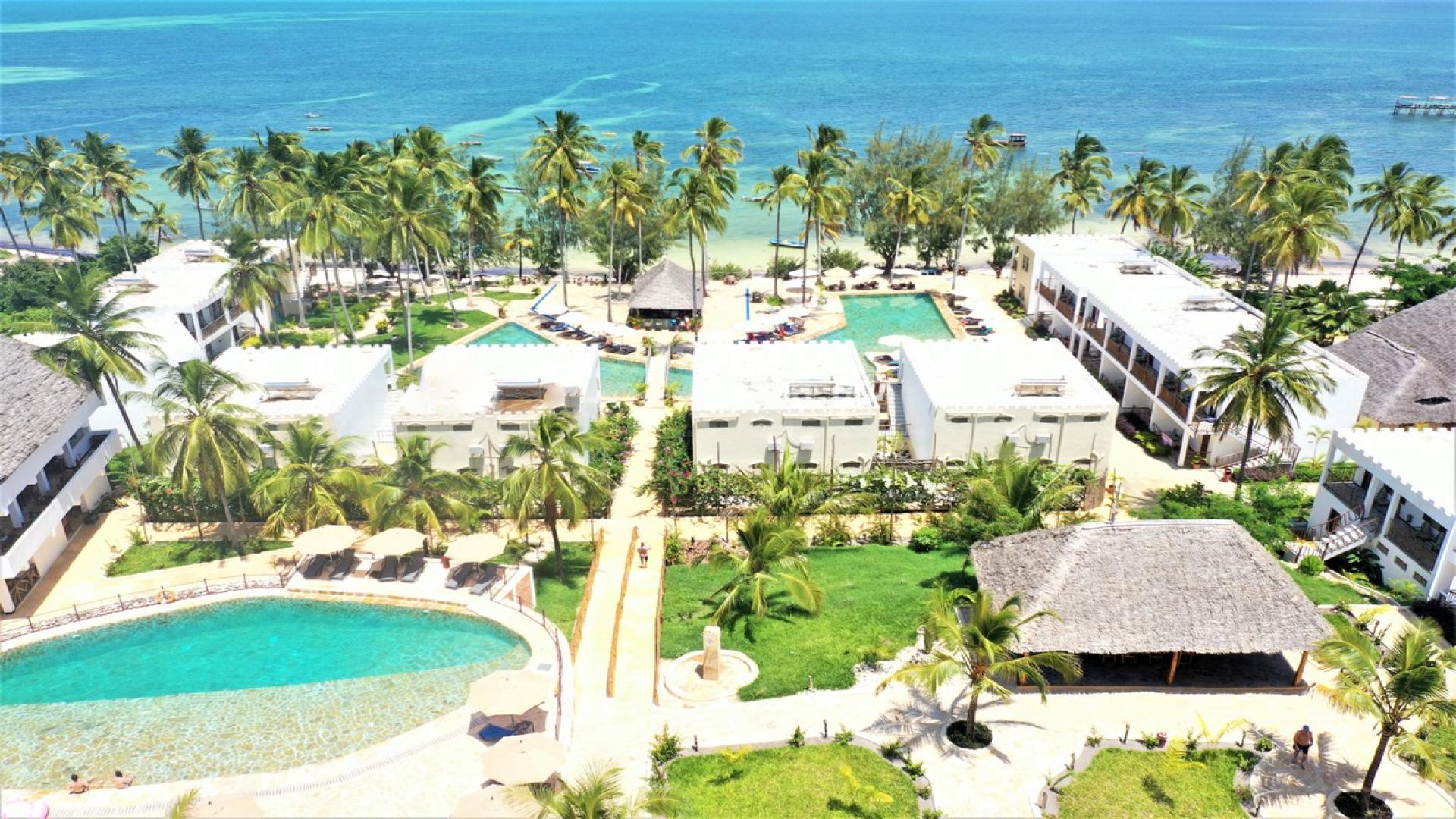 Aerial shot of the Zanzibar Bay Resort showing white hotel buildings with green palm trees in between all overlooking the crystal blue sea