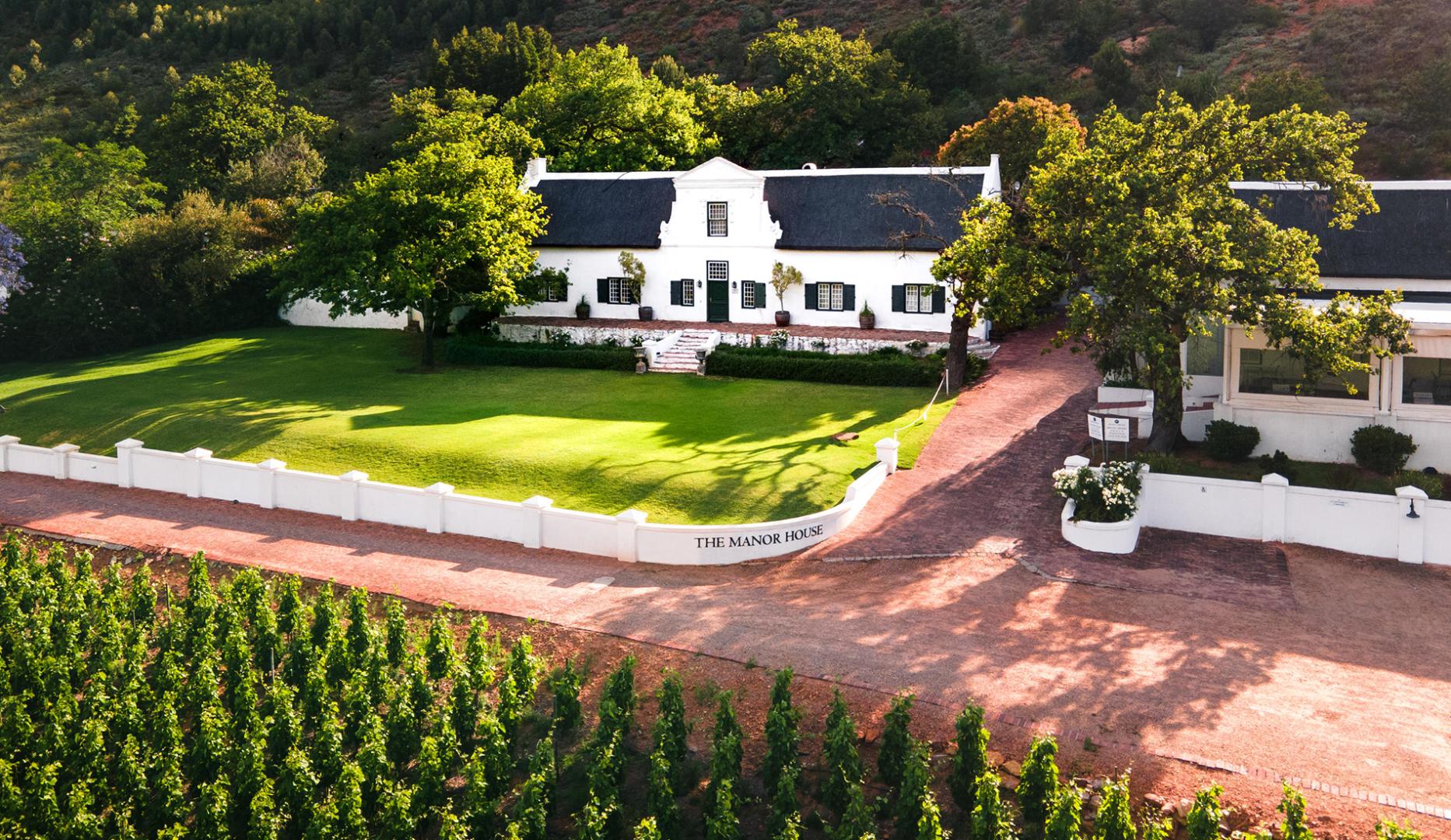 Wine Farm in Franschhoek, showing a white Manor house opposite a vineyard on a cool summer day. This is one of the cheap Easter getaways for 2025