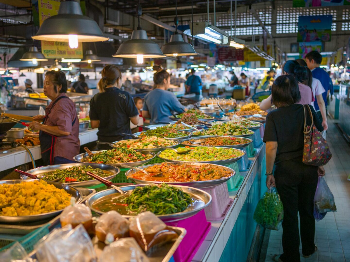 Food market in Bangkok with various Thai food platters. People and vendors are walking around. This is a must do activity for a Thailand on a budget trip.