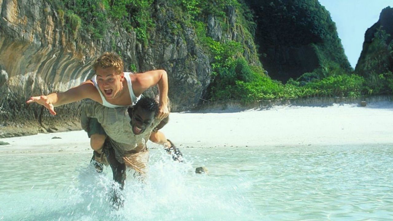Leonardo DiCaprio on Paterson Jospeh's back playfully running in the waters of Thailand's Maya Bay beach.  This movie is called "The Beach" and it was shot in Thailand