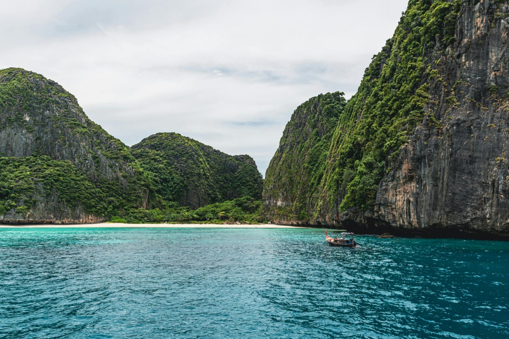 A view of the mountains and rock formations in Thailand. in the foreground there is a traditional Thai boat on crystal blue waters. This is one of the best holiday destinations for South Africans to visit in 2025 on Qatar Airways.