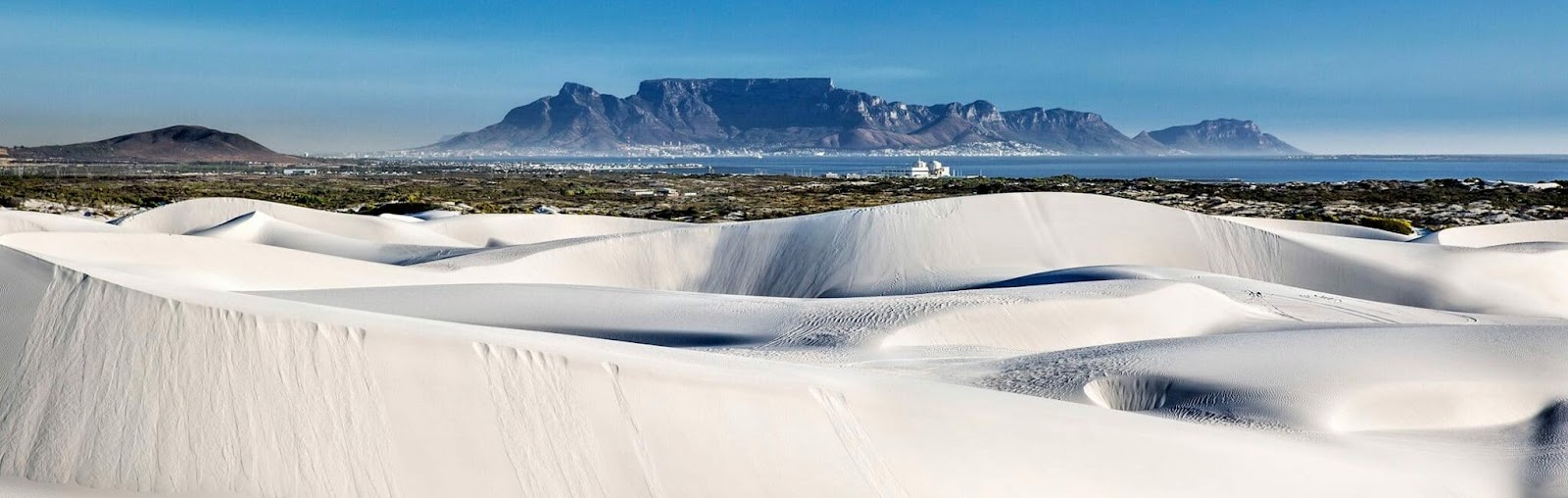 The atlantis dunes in Cape Town. White sand dunes in the foreground. and Table Mountain standing in the background. The sand dunes and the mountain are separated by the sea.