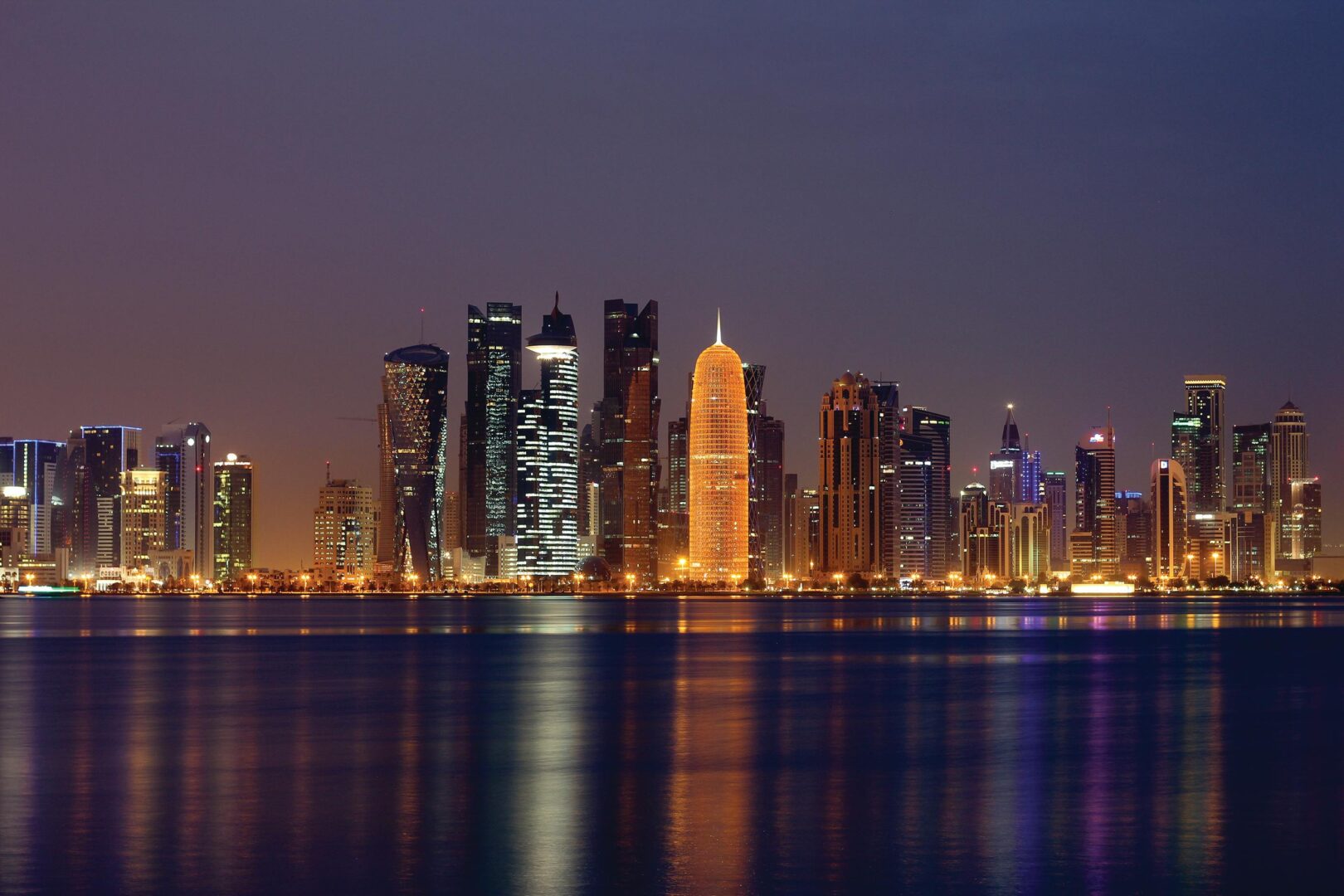Doha skyline showing skyscrapers lit up with various colours and the sea in the foreground. This what Qatar will look like during Ramadan 2025